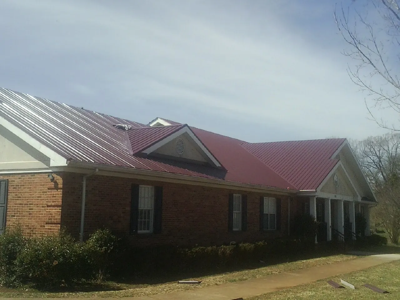 Red metal roof with gabled entries on a long brick building, from a Hail Damage Roof Repair job in Seaside